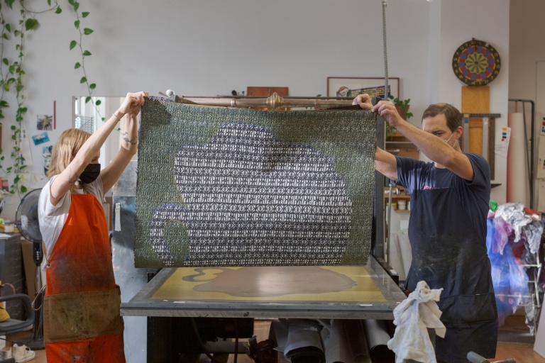 Printers Mackenzie Kimler and Justin Israels passing mesh material through the press with fabric.
